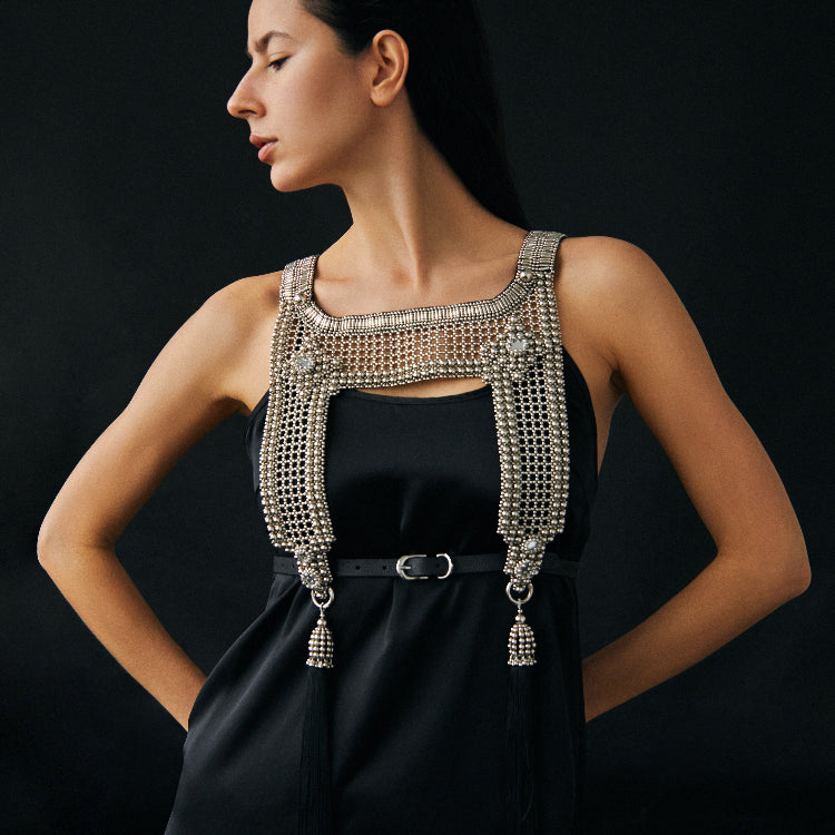 Woman wearing a black dress with a beaded silver harness against a dark background