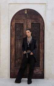 woman lean on the glass windows using V-Neck Beaded Harness w/ Collar Stand and Beaded Adjustable Chain Belt with Removable Tasselsilver in black outfit by object & dawn