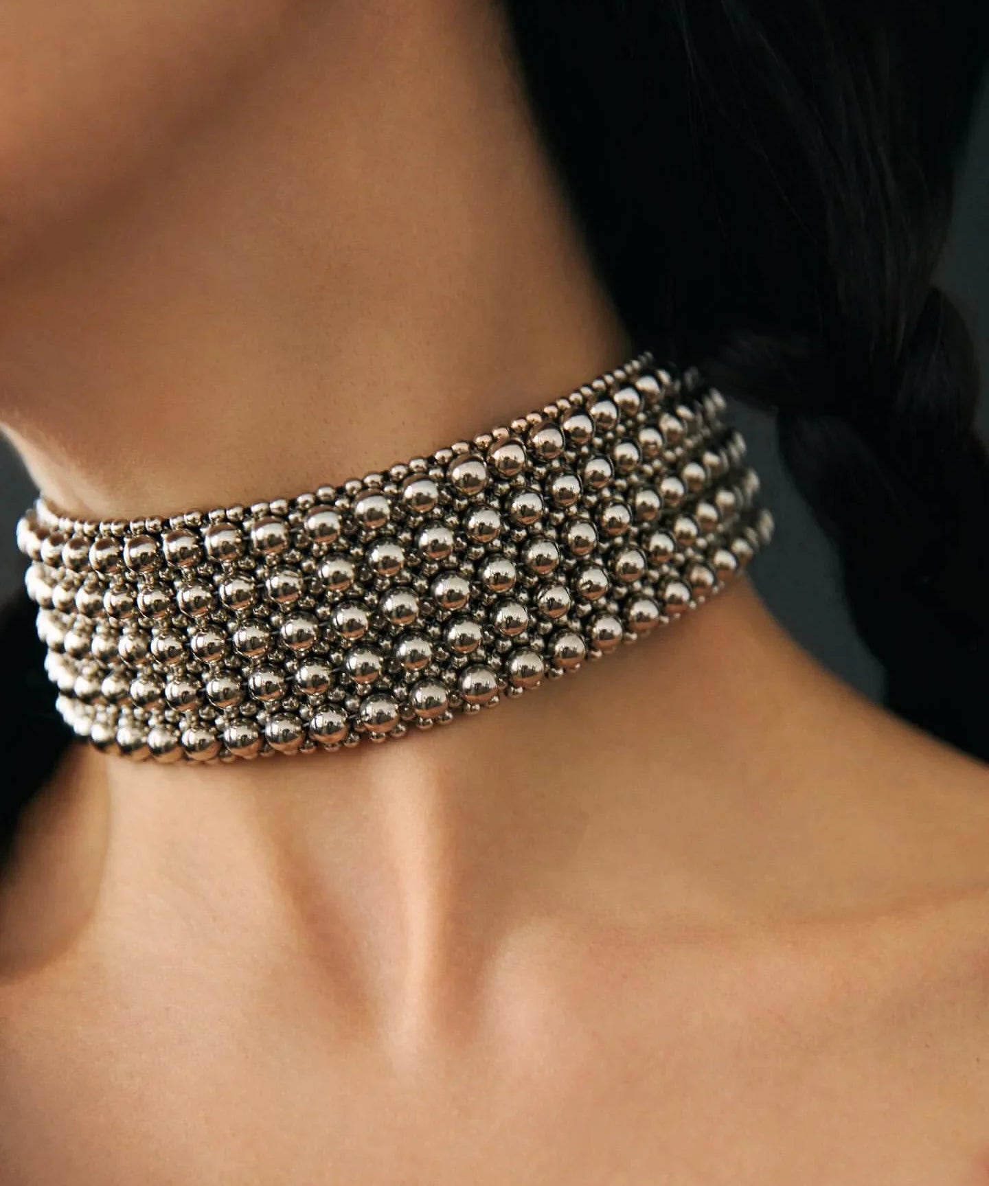 Woman wearing a silver choker against a dark background by object and dawn