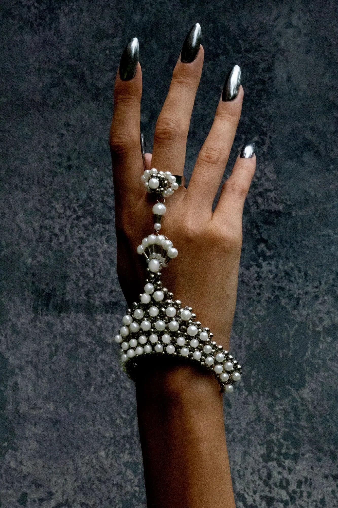 Hand wearing a decorative pearl bracelet and ring against a dark textured background