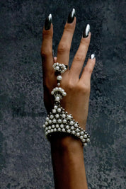 Hand wearing a decorative pearl bracelet and ring against a dark textured background