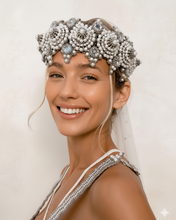 Woman wearing a decorative headpiece with pearls and mirros on a plain background