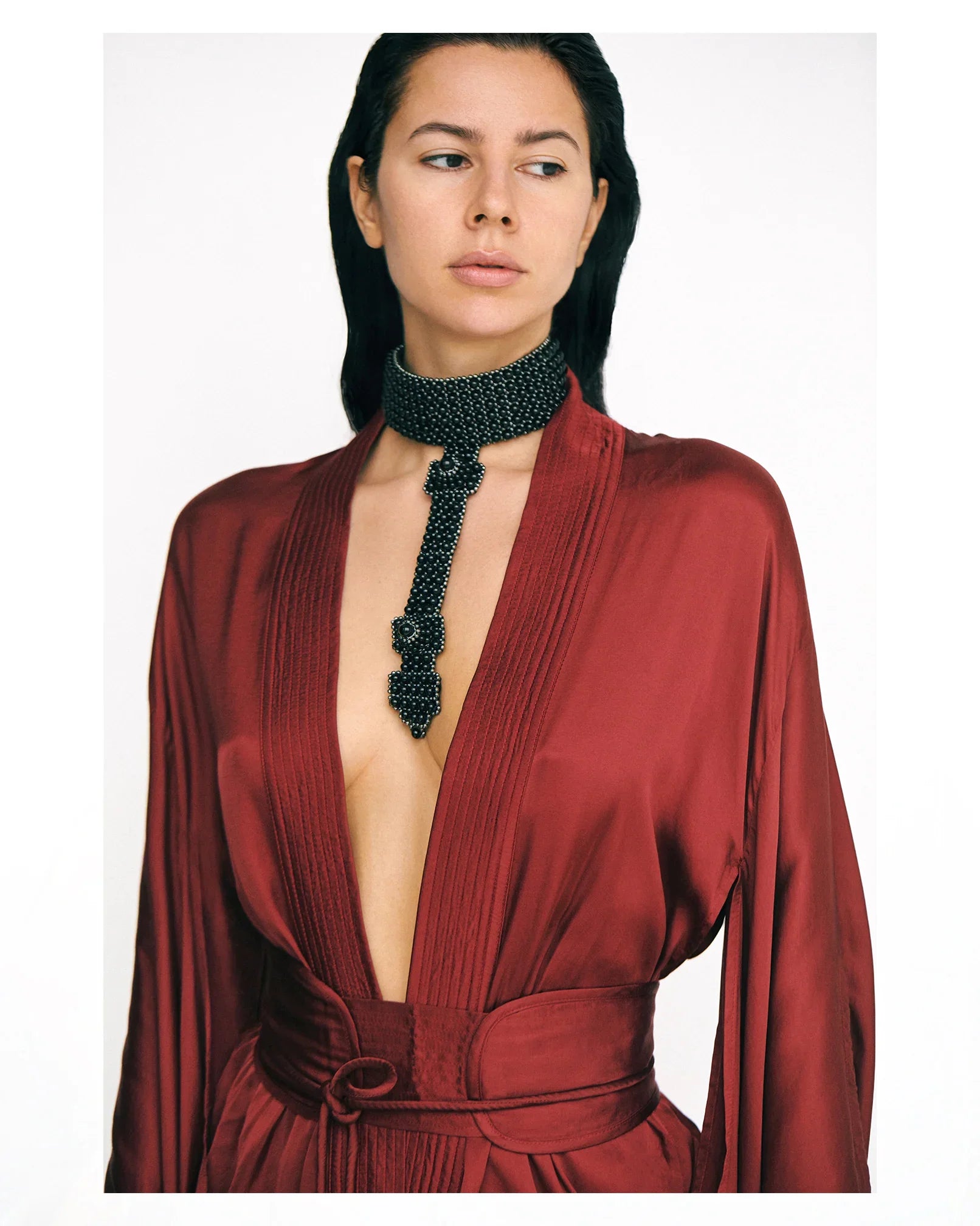 Woman wearing a burgundy short silk kimono and a black beaded necklace on a white background