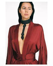 Woman wearing a burgundy short silk kimono and a black beaded necklace on a white background