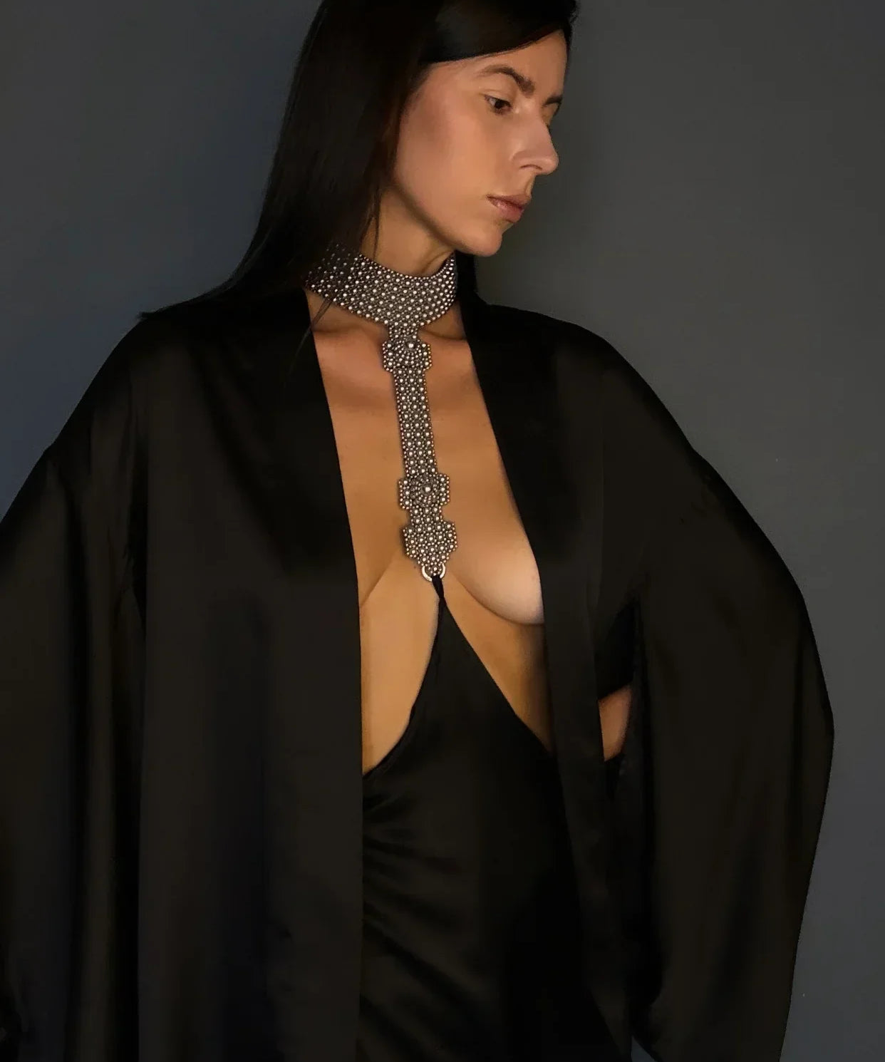 Woman wearing a black silk skirt connected to a silver beaded necklace against a gray background