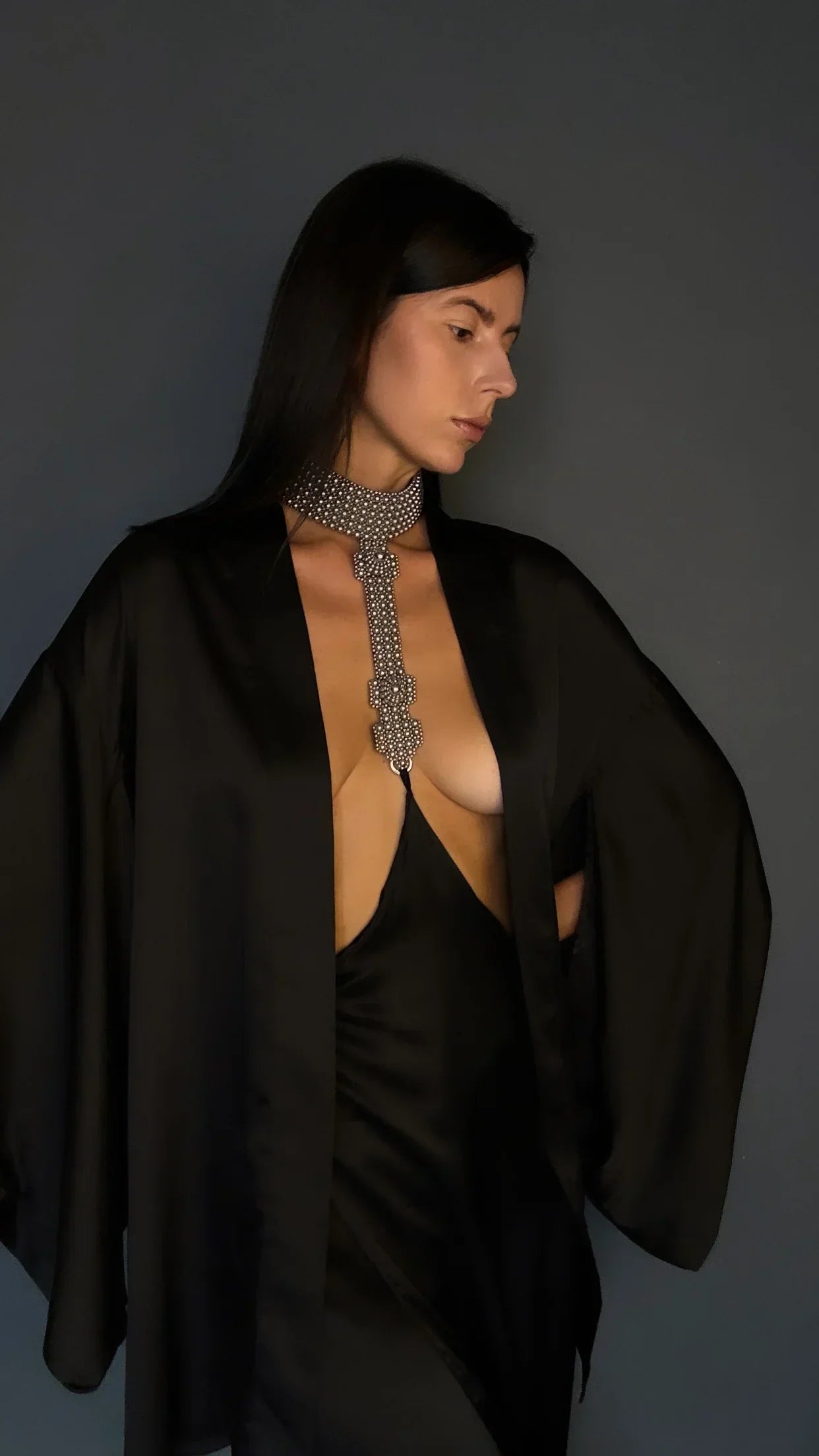 Woman wearing a black silk skirt connected to a silver beaded necklace against a gray background