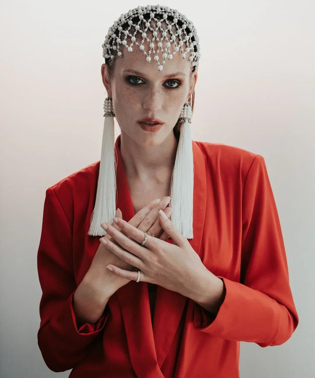 Woman wearing a red outfit with decorative headpiece and earrings against a plain background