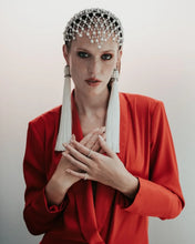 Woman wearing a red outfit with decorative headpiece and earrings against a plain background