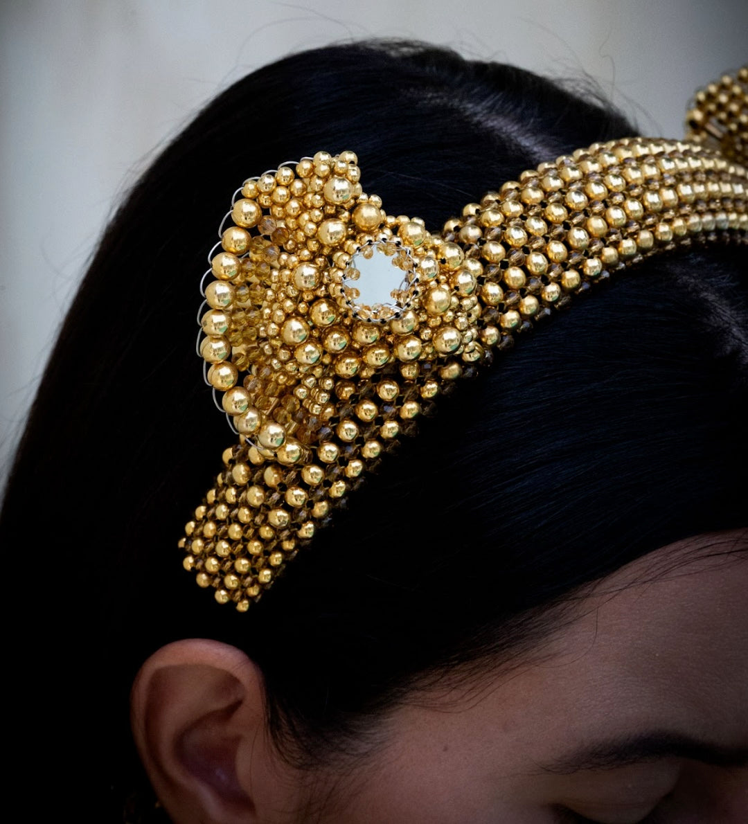 Gold beaded headband worn by a person with a neutral background