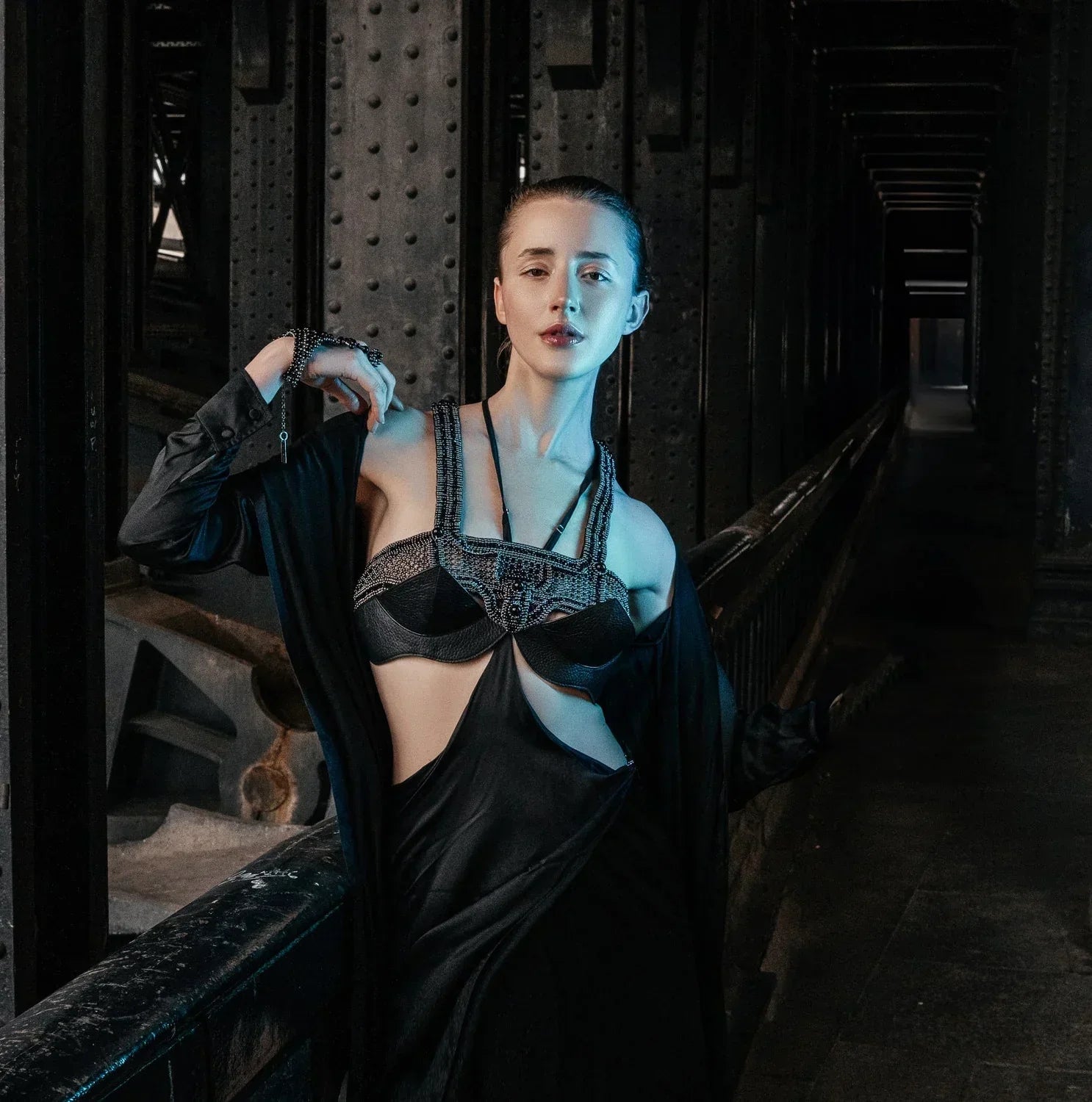 A woman wearing Object & Dawn beaded accessories in black with black silks clothing in a dark, industrial setting