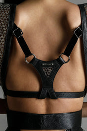 Close up of woman's back wearing Black leather harness on a neutral background