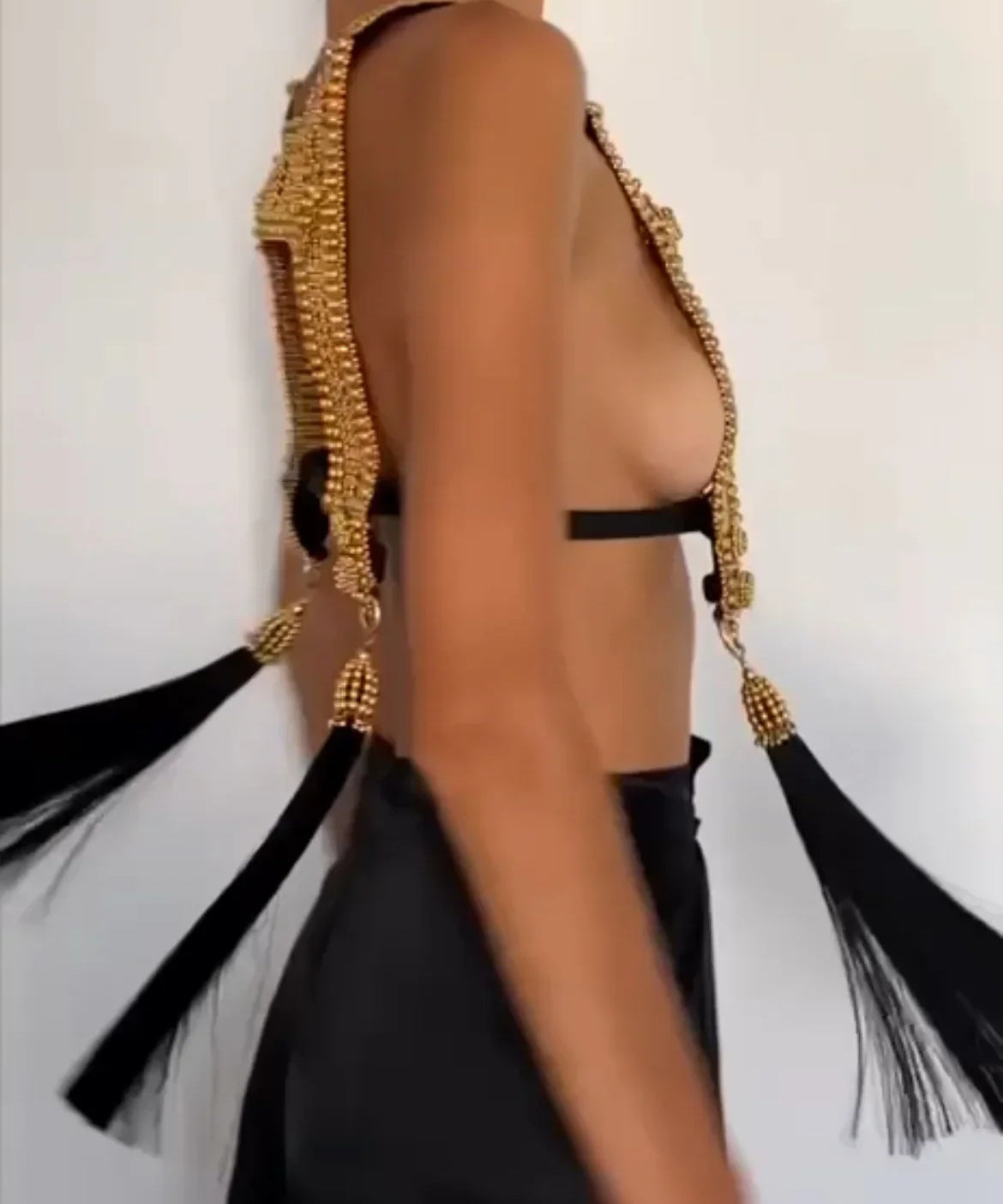 Torso of woman spinning while wearing gold beaded harness. Gold capped black threaded tassels float with spinnning motion. white background