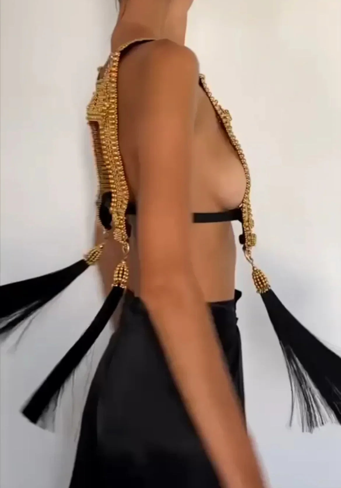 Torso of woman spinning while wearing gold beaded harness. Gold capped black threaded tassels float with spinnning motion. white background