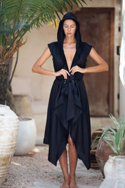 Woman wearing a black silk sleeveless robe with a hood in an outdoor setting.
