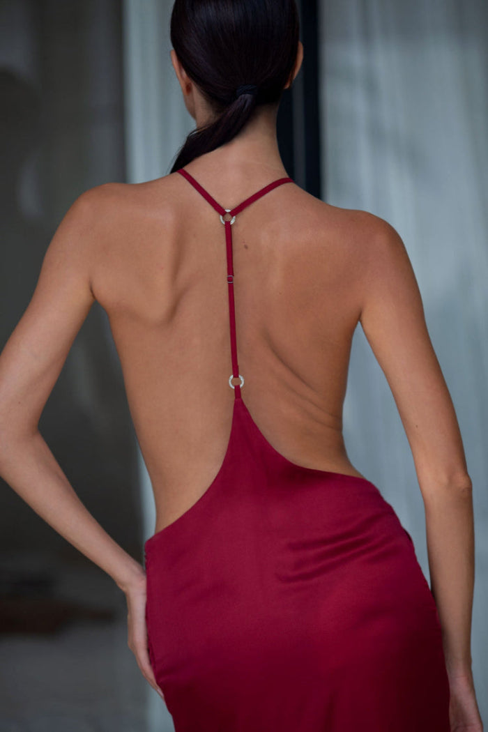 Woman wearing a burgundy dress with an open back, standing against a blurred indoor background.