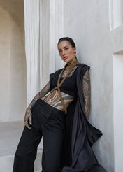 woman in black robe in long black pants wearing V neck beaded harness w collar antique gold by object & dawn in white building