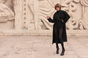Woman wearing a black outfit and V-Shape Beaded Harnessstanding in front of stone sculptures by Object & Dawn