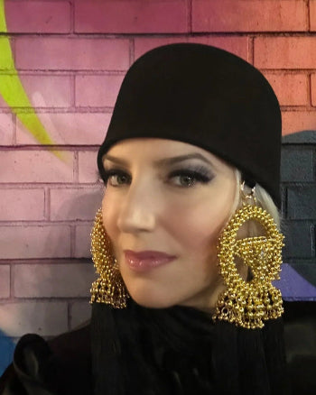 Woman wearing a black hat with gold tassels hanging on either side with a colorful brick wall background