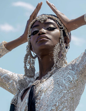 Woman wearing a sparkling outfit with silver beaded Rushi headpiece by Object & Dawn against a clear blue sky